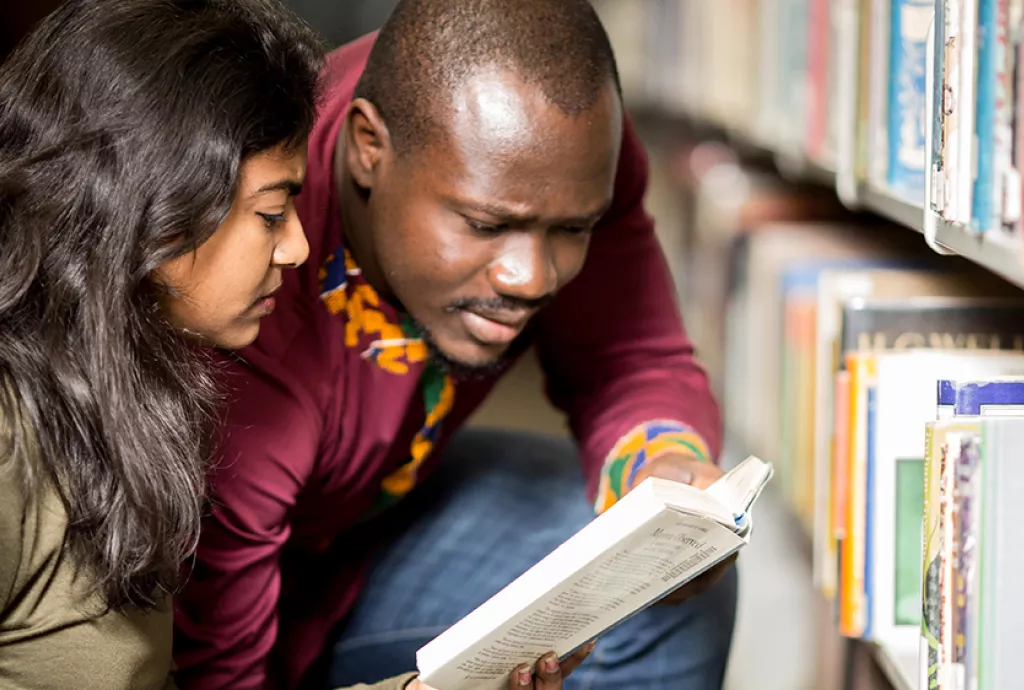 Three students sitting in the Confederation College Library, surrounded by books and studying.